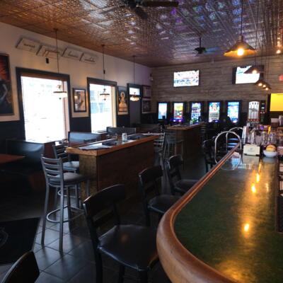 Spacious bar interior with high tables, barstools, televisions, and warm overhead lighting.