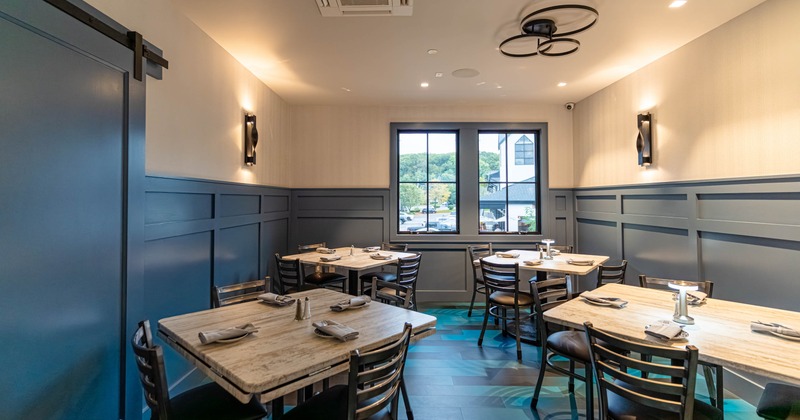 A modern dining room with wooden tables and chairs, blue wainscoting, and a large window