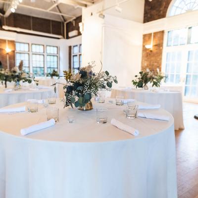 Round skirted tables with white table cloths, flowers, glasses, and napkins.