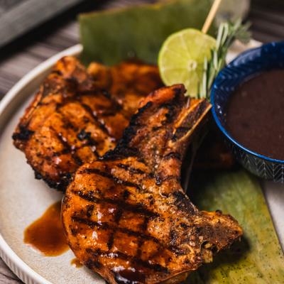 Grilled pork chops with dipping sauce and lime garnish.