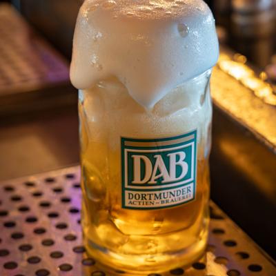 Glass of beer with foam overflowing it.