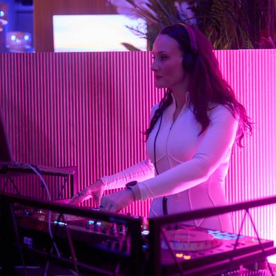 Outdoors, a person DJing at a booth under purple lighting.