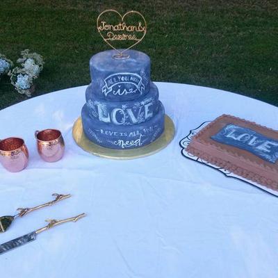A wedding cake on a table set with copper mugs and a dessert plate.