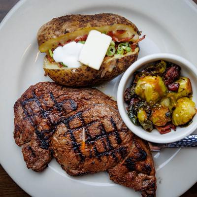 Grilled steak with a baked potato and roasted brussels sprouts.