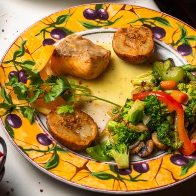 Grilled salmon with roasted potatoes and sauteed vegetables on a decorative plate.