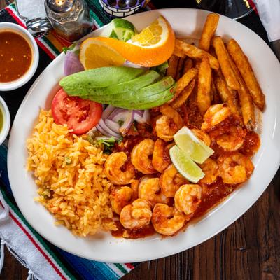 Mexican spicy shrimp served with rice, fries, salad, avocado, lime, and orange garnish.