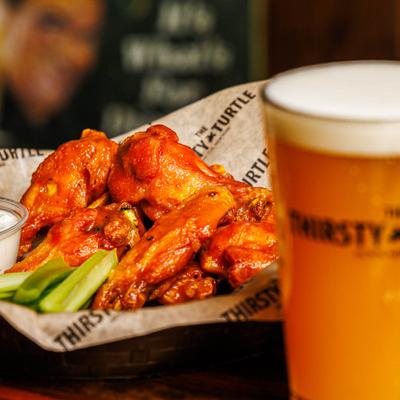 Basket of wings with celery stick and a dip, served alongside a glass of beer.