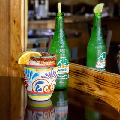 Cocktail in a clay cup, and a bottle of Jarritos soda.