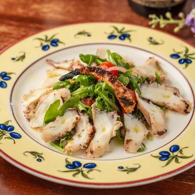Grilled octopus over arugula salad on patterned plate.