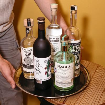 Tray with assorted mezcal bottles held beside a small table.