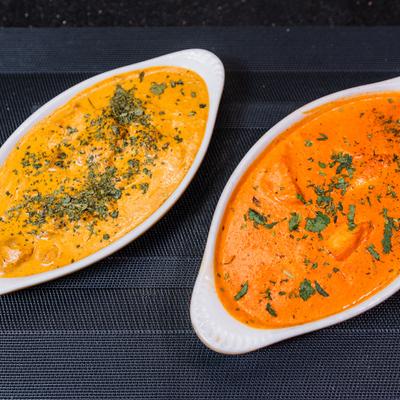Two curry dishes served in oval bowls, topped with herbs.