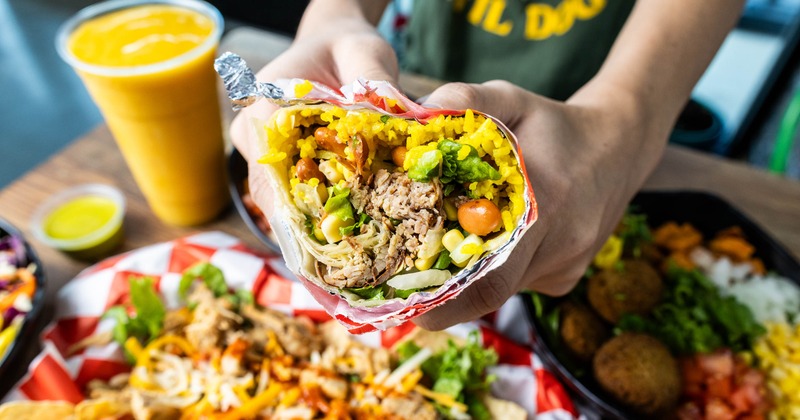 Person holding a burrito above the table filled with food