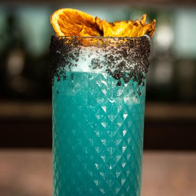 Cocktail served in a highball glass with a black rim and dried fruit garnish.