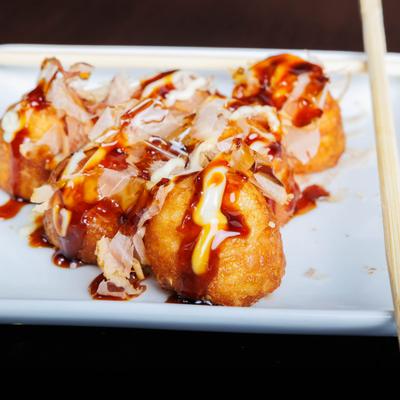 Japanese takoyaki topped with bonito flakes, mayo, and sauces on a white plate with chopsticks.
