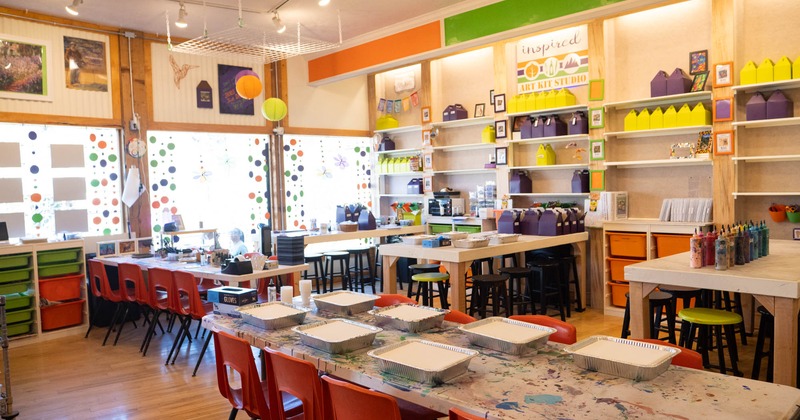 Brightly colored art studio with tables, chairs, and shelves full of craft supplies