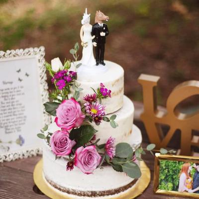 A two-tier wedding cake with floral decorations, framed pictures, and a  LOVE sign.