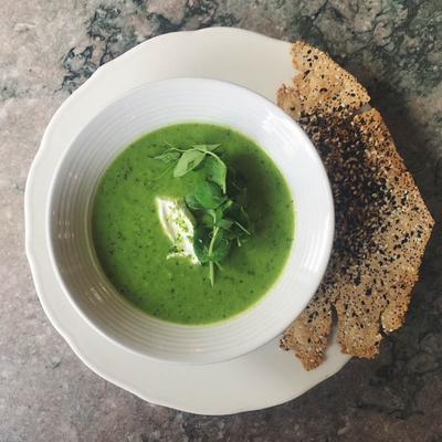 Green soup topped with a dollop of cream, served with crispy bread.