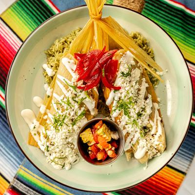 Tamales, with cheese, sour cream, pickled onions, cilantro, rice, and salsa.