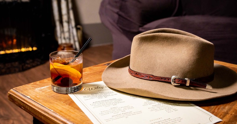 A armchair by the table with glass of bourbon and western hat on it.