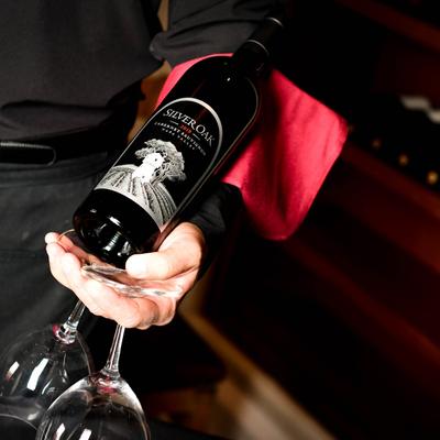 A wine bottle and two wine glasses held in one hand by a waitperson.