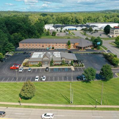 Aerial view of a commercial building with a parking lot and surrounding trees.