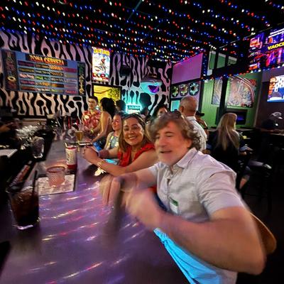 Man and woman sitting at a bar, little lights lining the cieling and a party atmosphere.