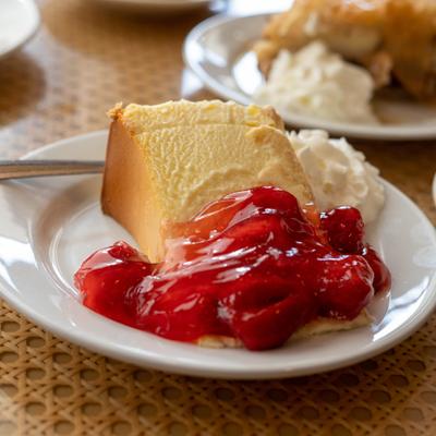 Slice of cheesecake topped with glazed strawberries and whipped cream.
