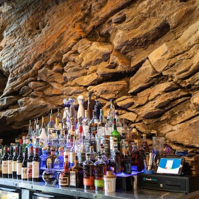 Bar table with spirits and wine bottles in front of a sedimentary rock wall.