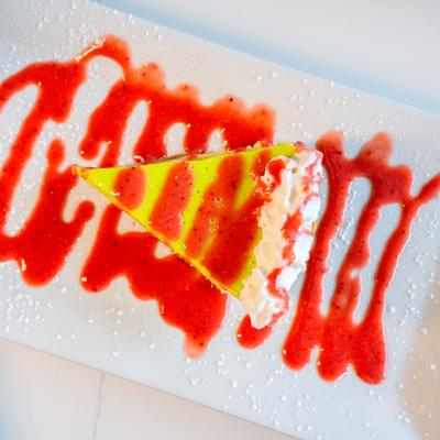 Strawberry cheesecake slice with red strawberry sauce and whipped cream.