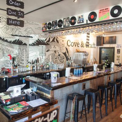 Trendy bar scene with a long counter, black stools, and colorful wall art of mountains and waves.
