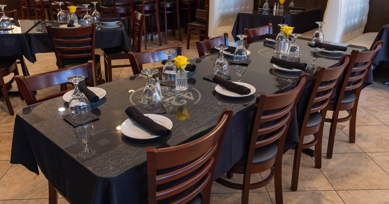 A restaurant dining area - a wooden table set with plates, black napkins and a yellow rose in a vase