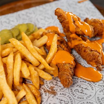 Chicken Tenders drizzled with sauce and served with fries.