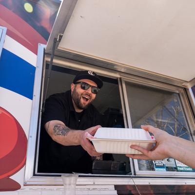 A friendly employee hands a food container to a customer from the food truck window.