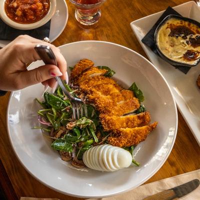 A hand holding a fork digging into a spinach salad with breaded chicken and egg slices.