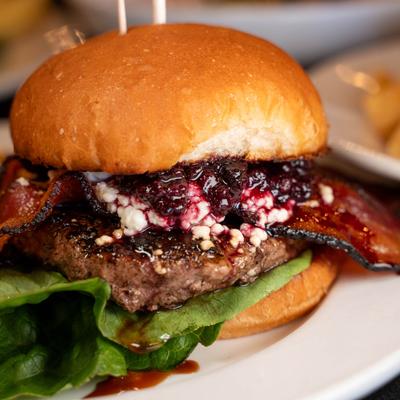 A gourmet burger - crispy bacon, a juicy beef patty, lettuce and berry jam, with French fries.