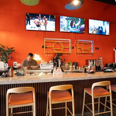 The bar area featuring orange walls, stools with orange seating, and TVs.