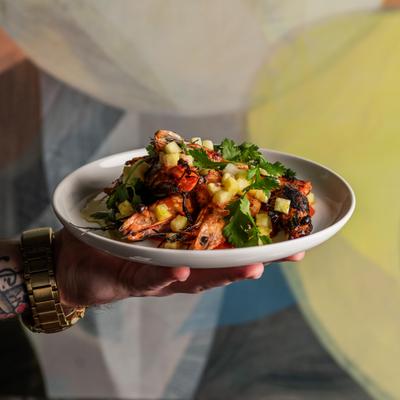 Plate of food with shrimp, fresh greens, and a savory topping being held by a person.