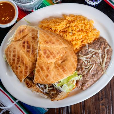 Mexican torta sandwich served with rice, refried beans, and a cup of red salsa.