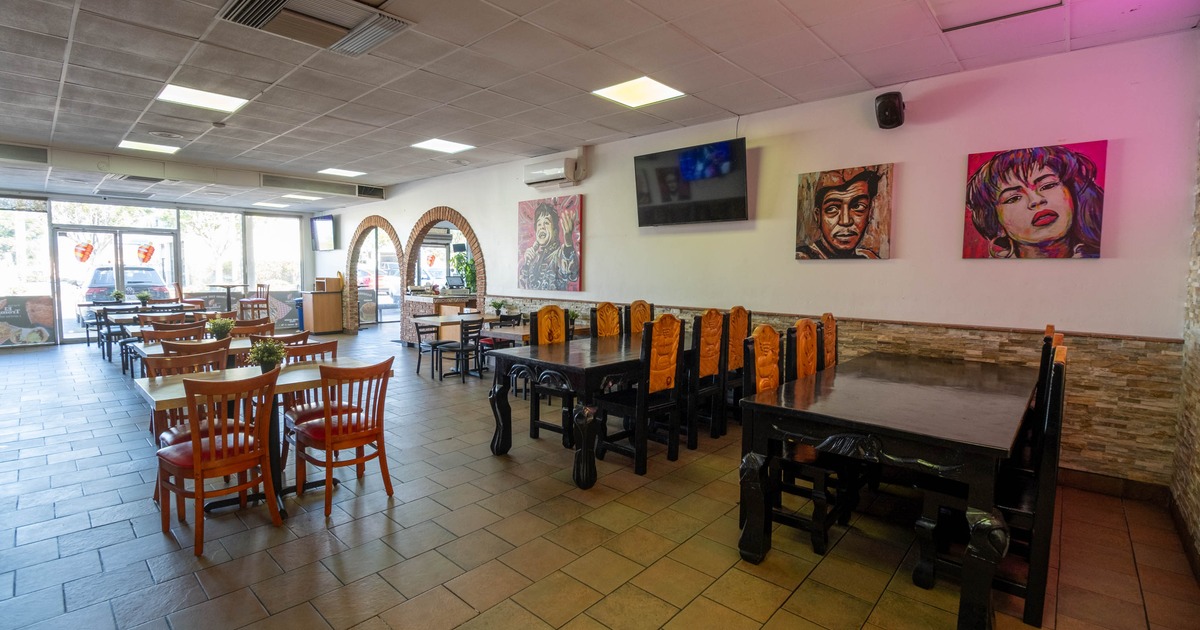 Interior with wooden tables and chairs, colorful paintings and a flat-screen TV