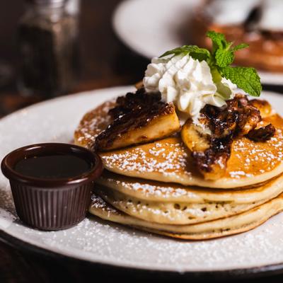 Stacked pancakes topped with caramelized bananas, whipped cream, and powdered sugar.