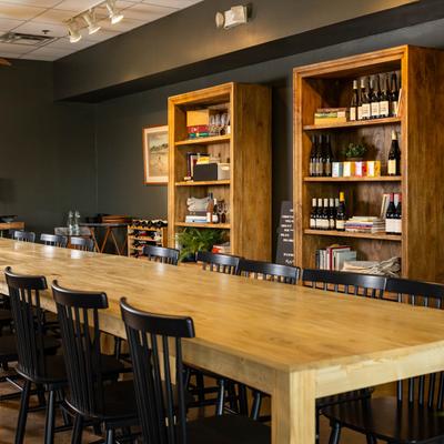 Interior, long wooden table setup with chairs, wooden shelves with wine bottles