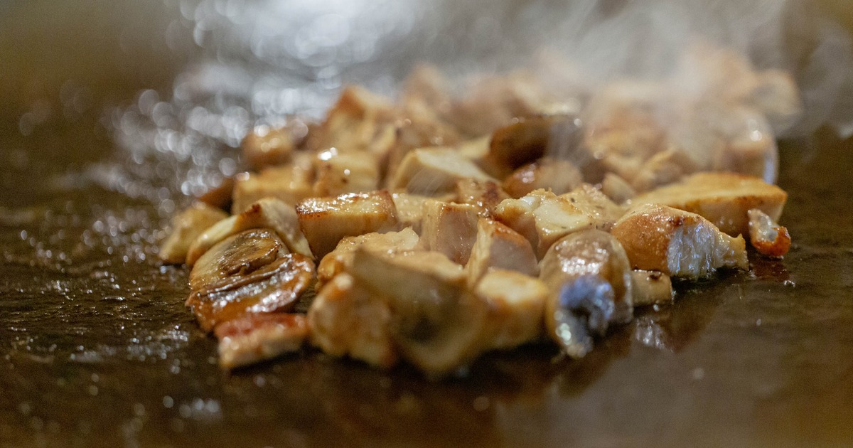 Chicken and mushrooms being prepared on a teppanyaki grill, close-up