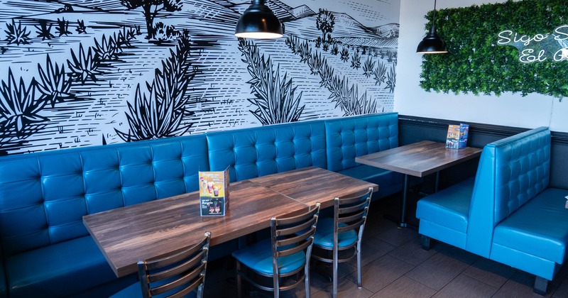A restaurant interior with blue tufted booths, wooden tables, a landscape mural