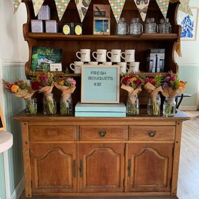 Rustic wooden hutch with fresh bouquets for sale, alongside various goods.