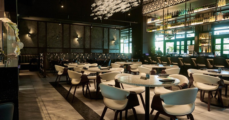 Interior, dining area, round marble top tables for four, bar in the back, tile flooring