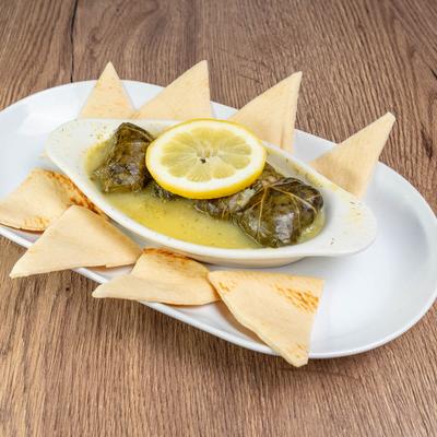 Stuffed grape leaves with lemon dill sauce, served on a white plate with pita bread.