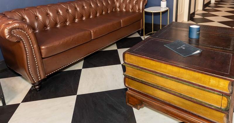 A brown leather sofa - a tufted back, a book-styled coffee table; checkered black-white floor