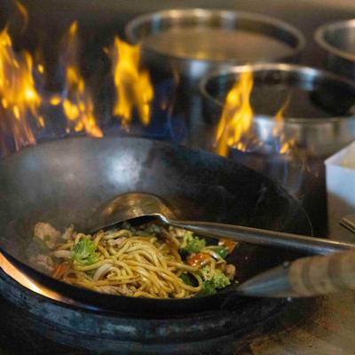 Stir-fry noodles with vegetables in a flaming wok.