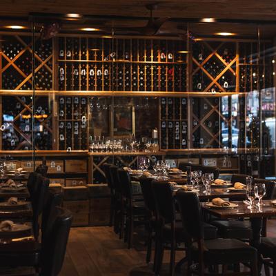 Restaurant dining tables in front of an illuminated wine wall.