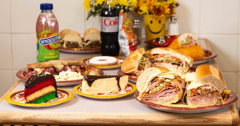 A table with sandwich plates, cake slices, snacks, and beverages on it